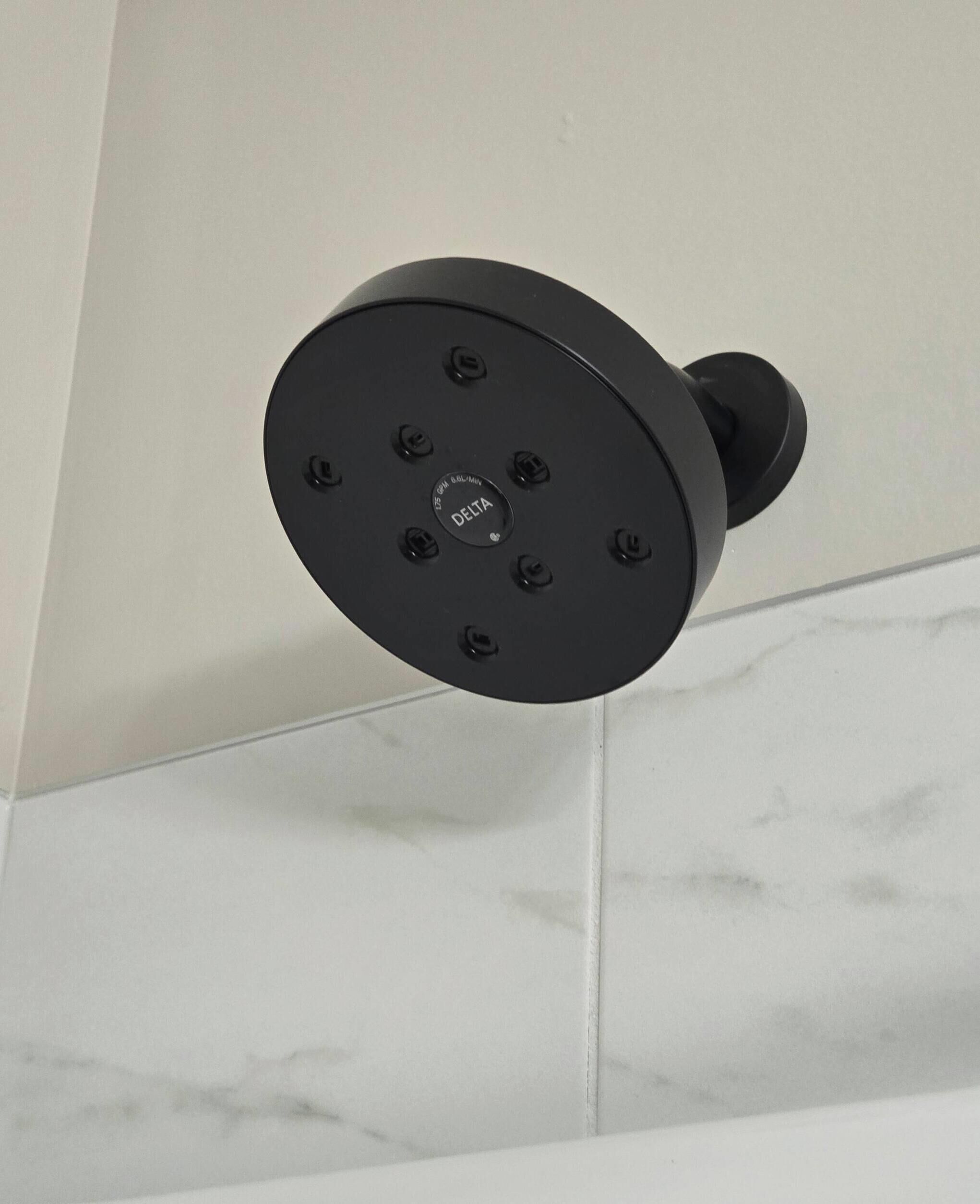 A black showerhead mounted on a white tiled wall.