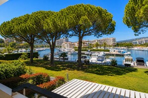 A marina with boats, a grassy area with trees, and buildings in the background. - Beautiful apartment, balcony with harbor view, sleeps 4 (Mandelieu-la-Napoule)