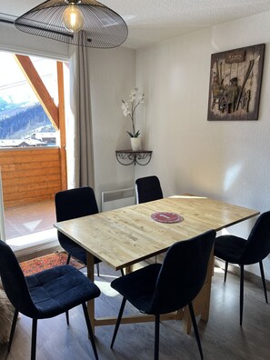 A dining area with a wooden table, black chairs, a potted orchid, a wall-mounted artwork, and a view of mountains through a window. - Spacious Family Duplex Apartment - Right on the slopes - Sleeps 9 (Allos)