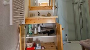 Un bany estret amb un moble prestatge integrat, un cubicle de dutxa amb envidriament i un mirall.