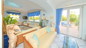 A living room with a sofa, coffee table, and a statue. There is a balcony with a view of the outdoors. - Hotel Terme Felix (Ischia)