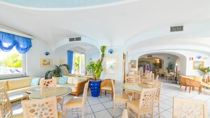 A spacious hotel lobby with a round glass table, multiple seating areas, and a view of the outdoor area. - Hotel Terme Felix (Ischia)