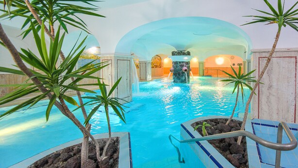 An indoor pool with clear water, surrounded by plants and a stone wall. - Hotel Terme Felix (Ischia)