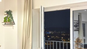 Ein Zimmer mit einer Schiebetür zum Balkon, einer kleinen Ablage mit Pflanzen und einem Essbereich, der durch die Tür sichtbar ist.