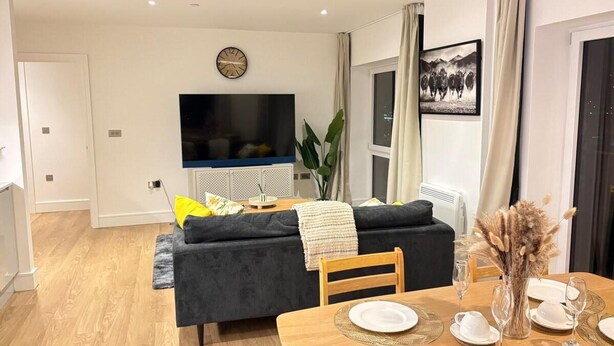 Ein modernes Wohnzimmer mit einer Couch, einem Esstisch für vier Personen, einem Flachbildfernseher und einem großen Fenster.