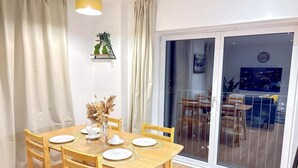 Ein Essbereich mit einem Holztisch, gedeckt für vier Personen, einer Vase mit Trockenblumen und einer Glastür, die auf einen Balkon mit Stadtblick führt.