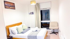 Ein Hotelzimmer mit einem Holzbett, einem Sessel, einem Fenster mit Vorhängen und einem Gemälde an der Wand.