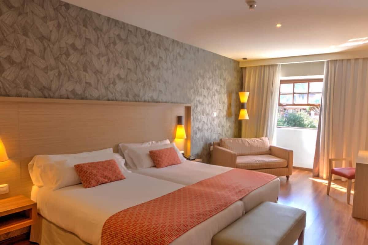 Una habitación de hotel con una cama grande, un sofá, una silla y una ventana con cortinas.