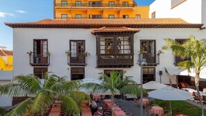Un immeuble à la façade blanche, doté de nombreux balcons et d’un espace extérieur aménagé avec des parasols.