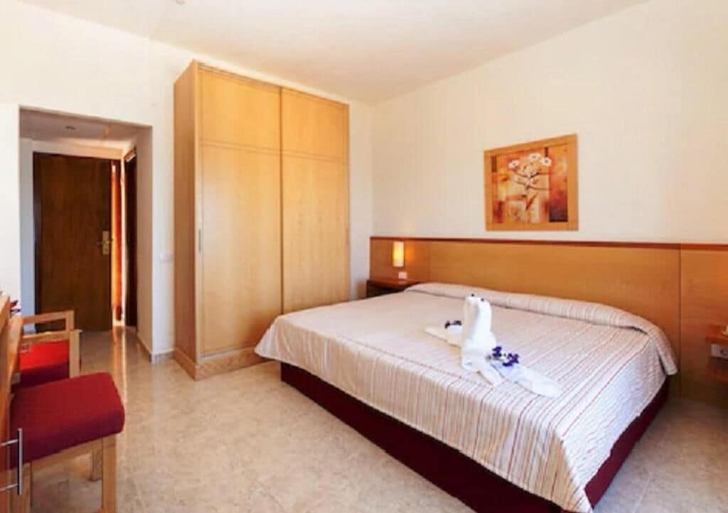 Habitación de hotel con cama, armario de madera, un cuadro en la pared y una silla roja.