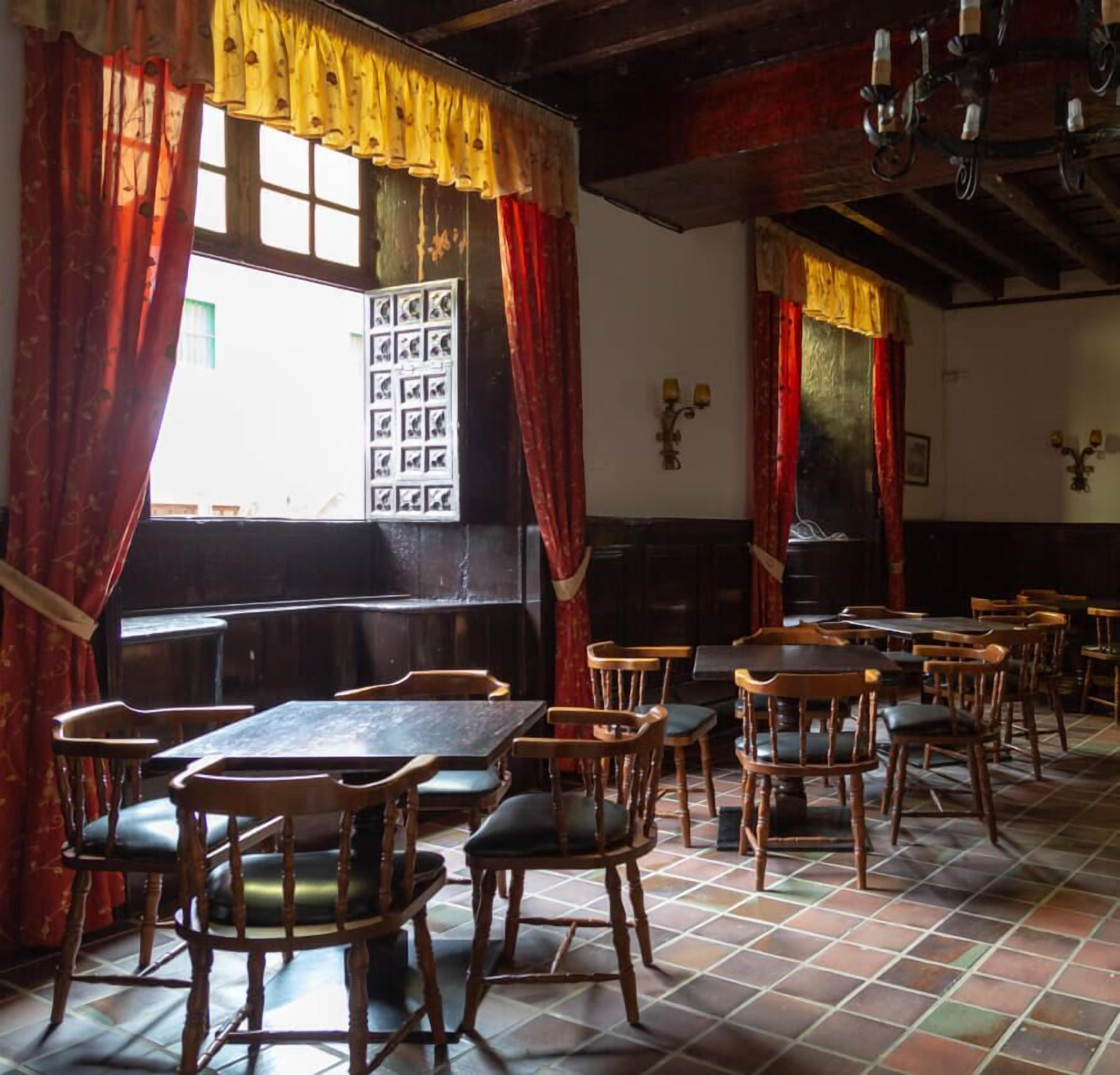 L’intérieur d’un restaurant avec des tables et des chaises en bois, des rideaux rouges et un sol carrelé.