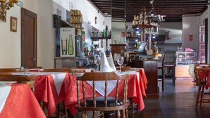 Un restaurant avec des tables et des chaises en bois, un coin bar et une cuisine visible au fond de la salle.