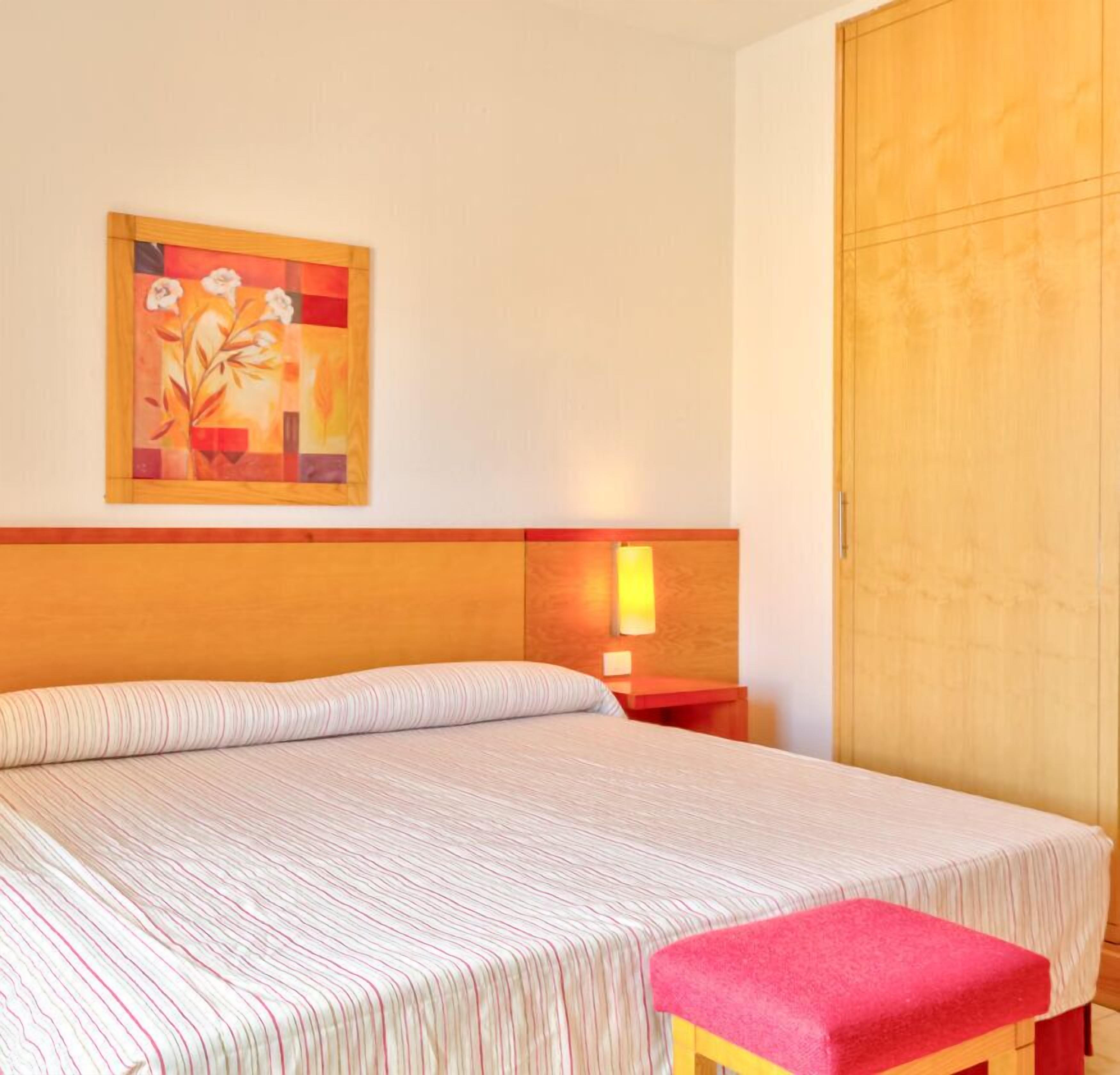 Une chambre d’hôtel avec un lit, une table de chevet, une lampe, une armoire en bois et un tableau au mur.