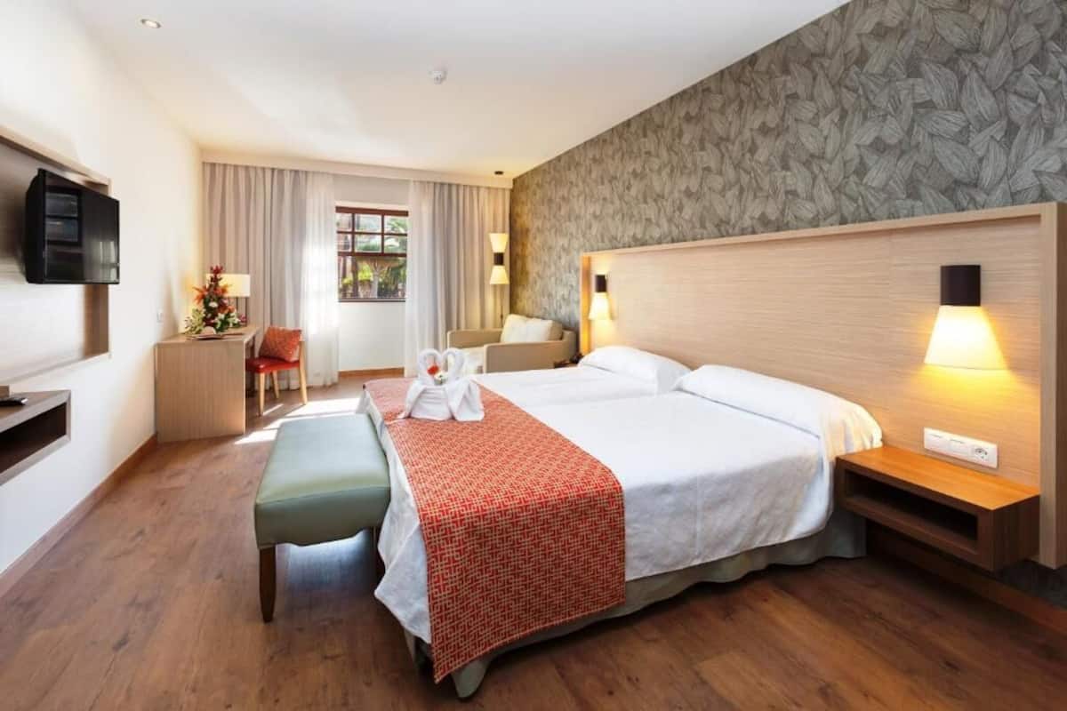 Una habitación de hotel con una cama grande, un escritorio, una silla, un televisor y una ventana con cortinas.