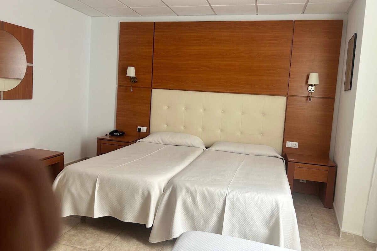 Una cama doble con cabecera de madera y dos mesitas de noche, cada una con una lámpara.