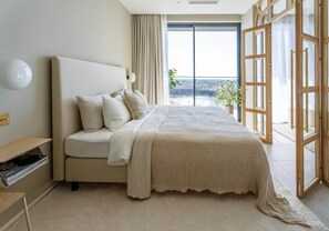 Un dormitorio con una cama grande, una mesita de noche, una lámpara y vistas a través de una puerta corrediza de vidrio.
