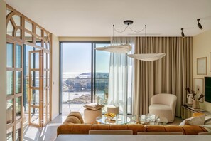 Ein modernes Hotelzimmer mit großem Fenster, einer Couch, einem Glastisch und einer Pendelleuchte.