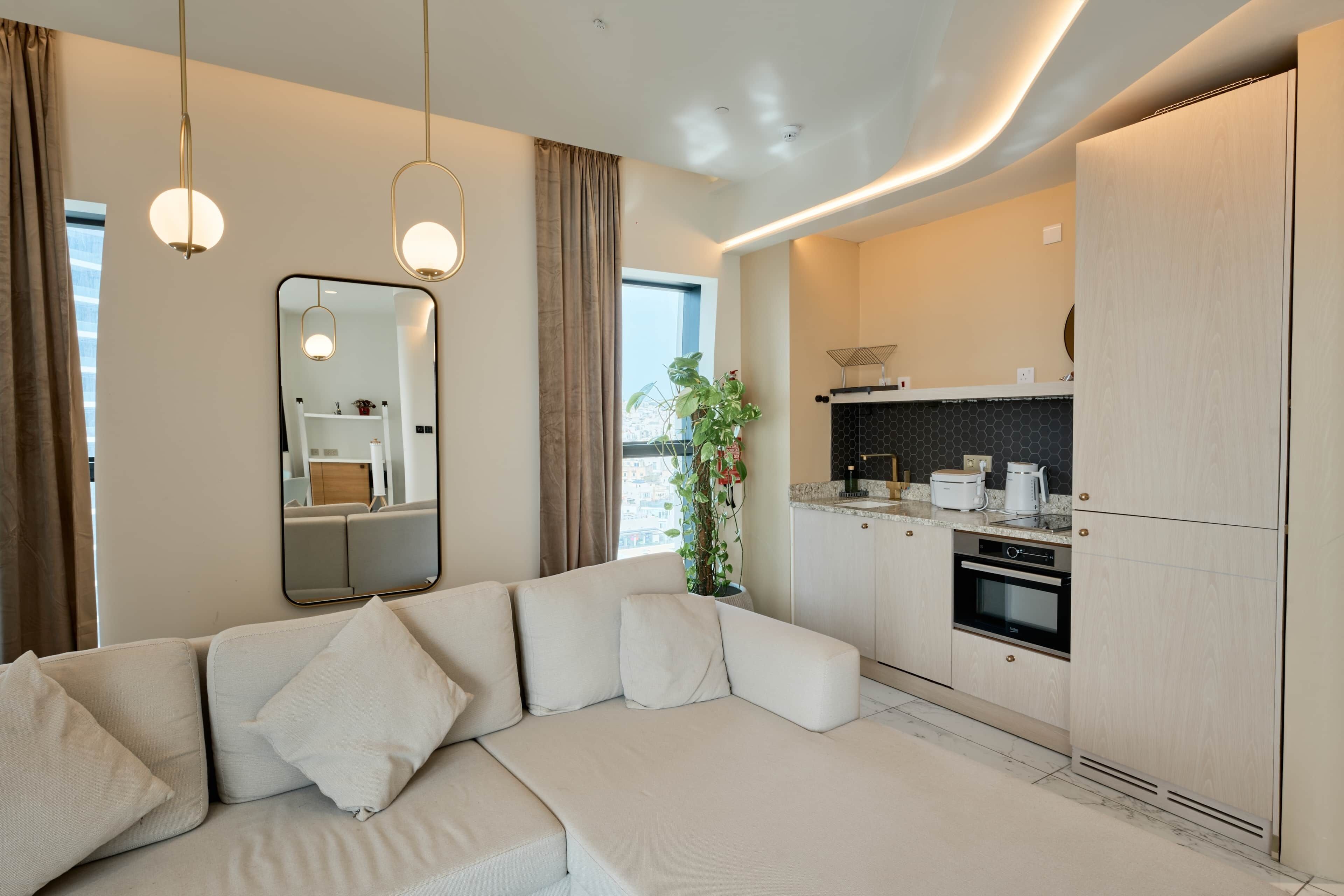 Un salon moderne avec un canapé, une cuisine équipée d’une cuisinière et une grande fenêtre.