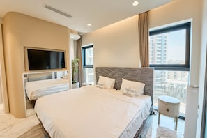 A modern hotel room with a large bed, a flat-screen TV mounted on the wall, a potted plant, and a view of the city through large windows. - Seaview Mercury Tower Apartment With Rooftop Pool (Saint Julian's)