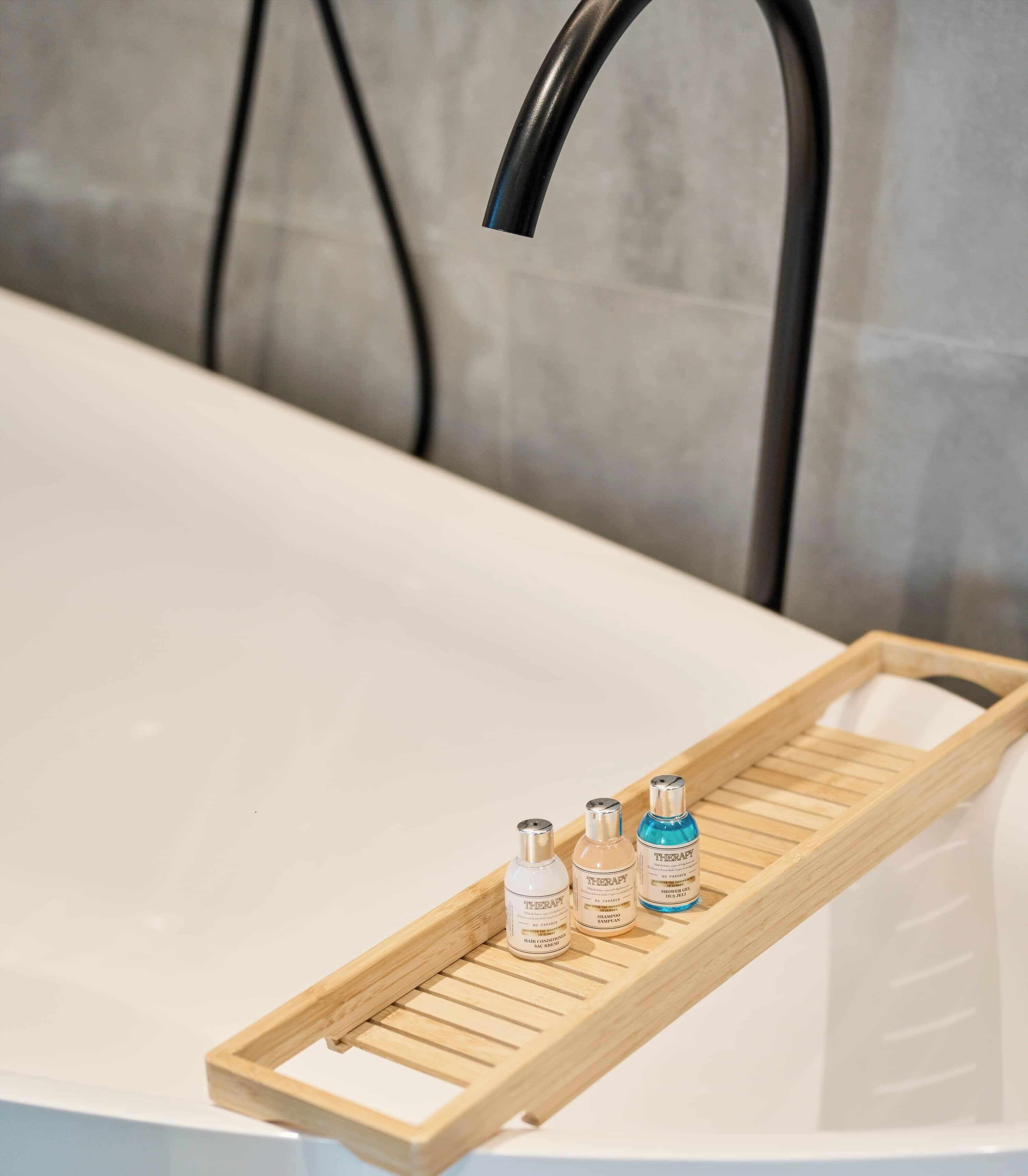 A bathroom with a white bathtub, a wooden tray holding three bottles, and a black faucet.
