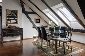 Ein Essbereich mit einem Glastisch, schwarzen Stühlen, einem gemusterten Teppich, einer Holzkommode und einem Bild an der Wand.