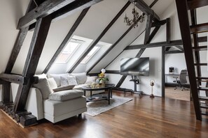 Ein Loft-Zimmer mit freiliegenden Holzbalken, einer Couch, einem Couchtisch, einem Fernseher und einem Schreibtisch mit Stuhl.