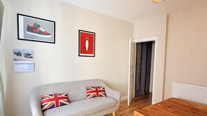 A room with a grey sofa, a wooden table, a framed shoe artwork, a calendar, and a door. - Modern 2BR Home w/Driveway | Sleeps 6 (Lincoln)