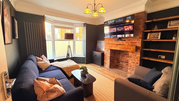 A living room with a sofa, armchair, fireplace, TV, and bookshelf. - Modern 2BR Home w/Driveway | Sleeps 6 (Lincoln)