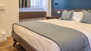 A modern bedroom with a large bed, a window with sheer curtains, a dark blue accent wall, and a built-in bench. - Blue Pearl - Grey Pearl Suites (Manfredonia)