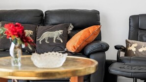 A black leather sofa with decorative pillows, a small round wooden table with a vase of flowers, and a chair with a cushion. - The Lookout Newhaven (Newhaven)