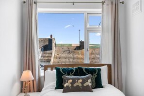 Une chambre à coucher avec un lit, des oreillers, une table de chevet et une fenêtre avec des rideaux.