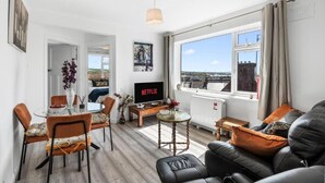 A modern living room with a TV, seating, a dining area, and a large window with a city view. - The Lookout Newhaven (Newhaven)