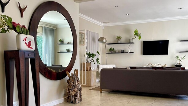 A modern living room with a large mirror, a sofa, a flat-screen TV, and decorative plants. - Hout Bay Gem 61 Milner  (Cape Town)