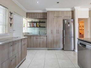 A modern kitchen with wooden cabinets, a stainless steel refrigerator, and a tiled floor. - Hout Bay Gem 61 Milner  (Cape Town)