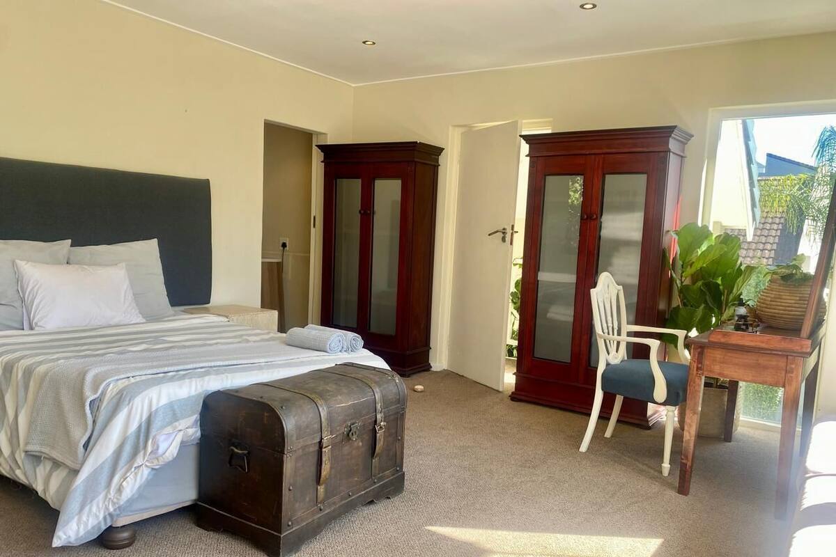 Um quarto com uma cama, uma cadeira, uma escrivaninha e um baú grande.