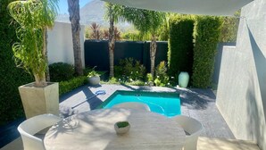 A round table with four chairs and a small potted plant in the center, surrounded by a pool and greenery. - Hout Bay Gem 61 Milner  (Cape Town)