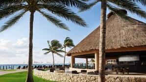 A resort with a thatched-roof structure, outdoor seating, and a view of the ocean. - Ocean-View 2BR Villa at Westin Lagunamar – Cancún Beachfront Pools & Spa (Cancún)