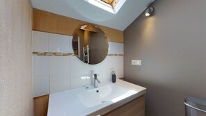 A bathroom with a skylight, a round mirror, a white sink, and a wooden vanity. - STRING (Sainte-Foy-de-Longas)