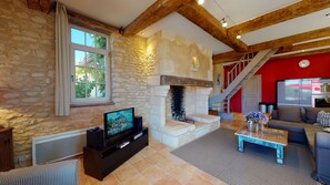 Ein Wohnzimmer mit Kamin aus Stein, einem Fernseher, einer Couch und einer Treppe.