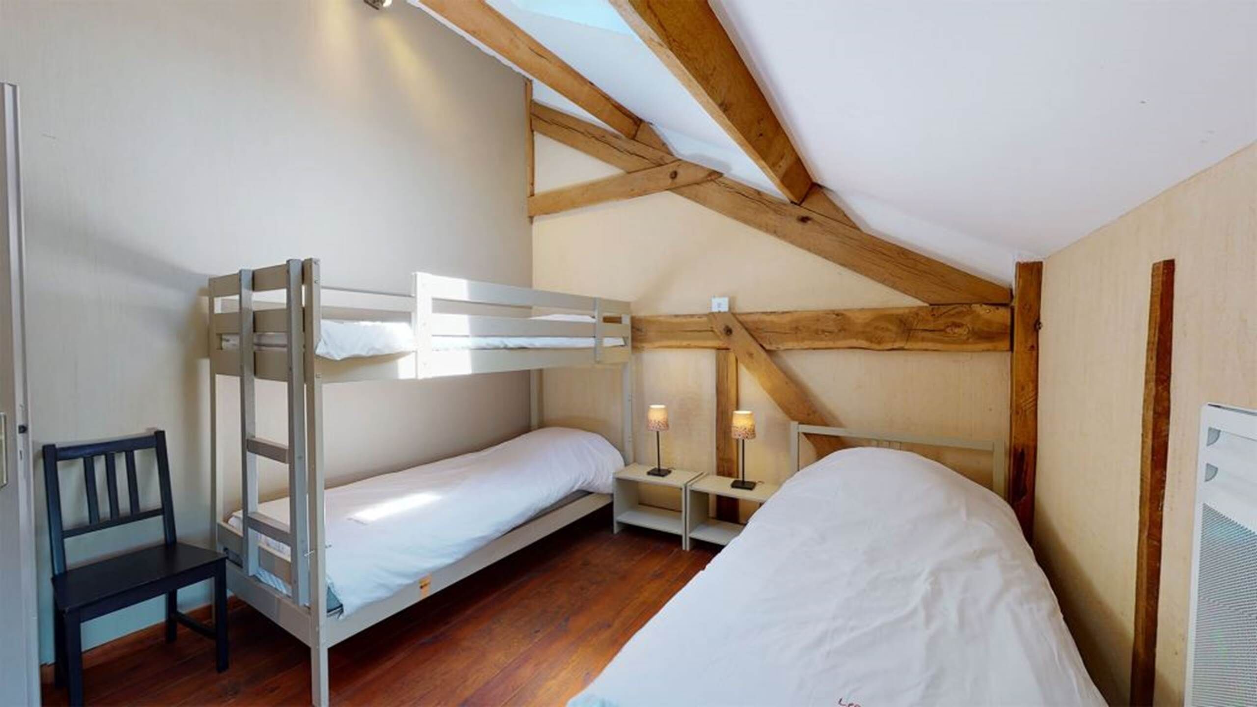 Ein Schlafraum mit Etagenbetten, Holzbalkendecke, Schreibtisch und zwei Nachttischlampen.