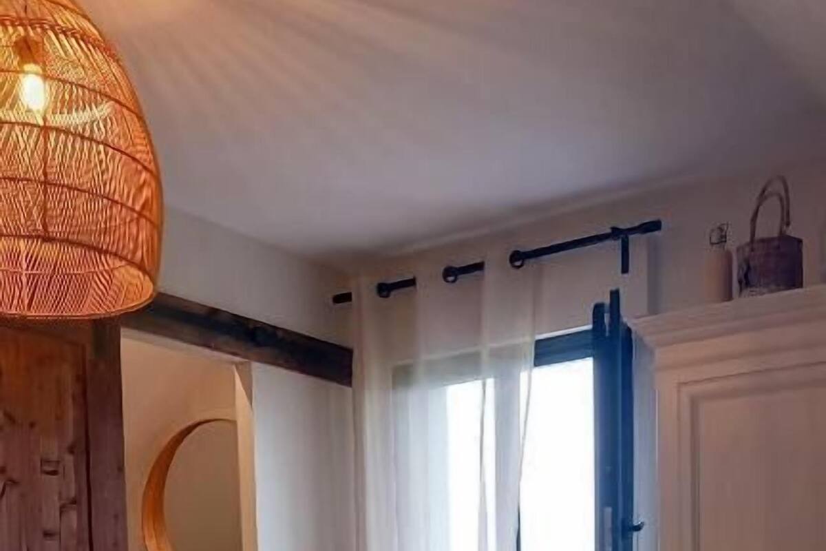 A bedroom with a bed, a hanging light fixture, a window with curtains, and a mirror.
