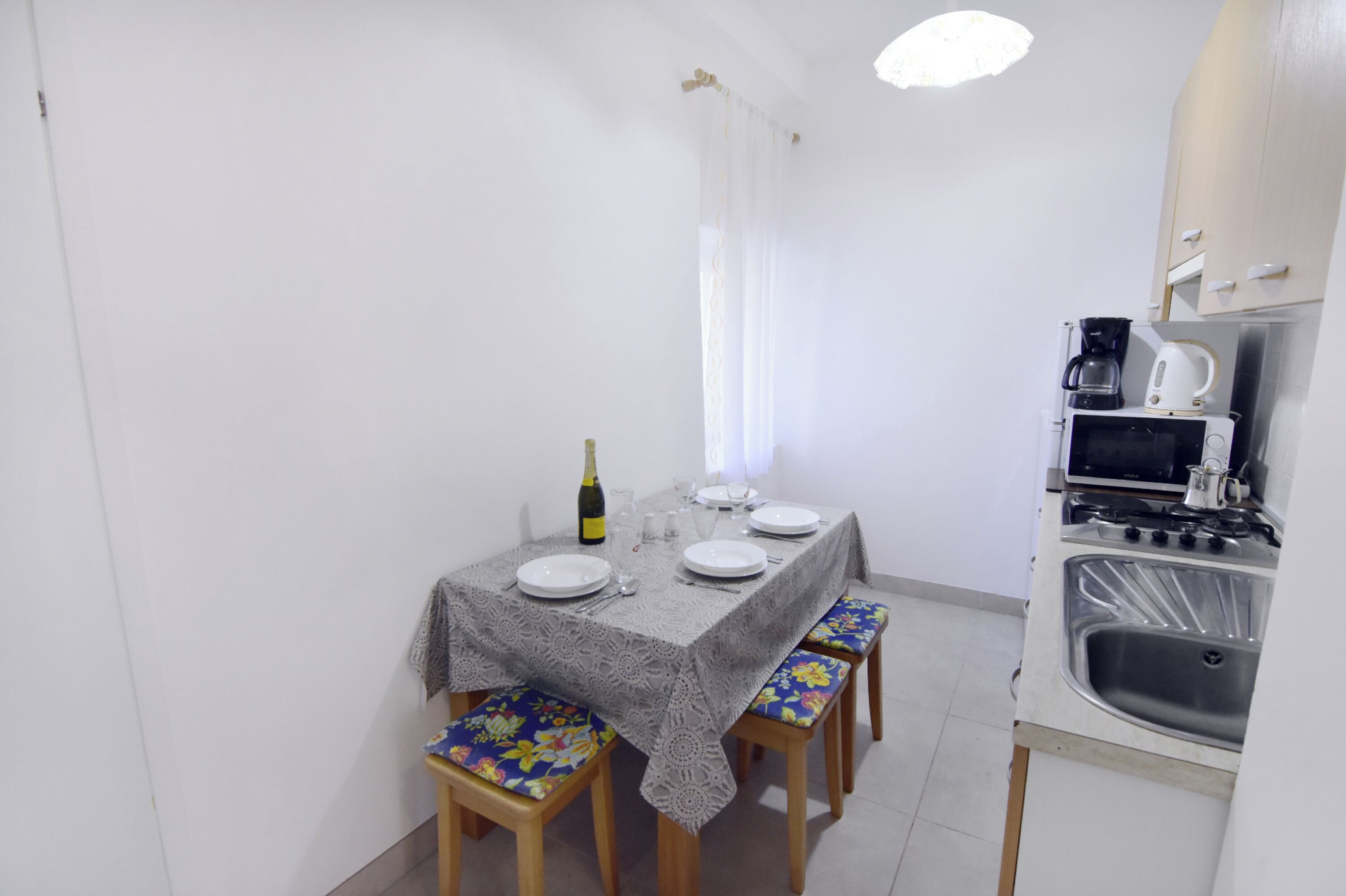 Spiseområde med et bord dækket til to, champagneflaske og et køkken med vask og hårde hvidevarer.