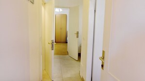 A narrow hallway with white walls and doors leading to a room with a wooden floor. - Practical Family Stay With Outdoor Area (Umag)
