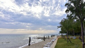 A pebbled beach with lounge chairs and umbrellas, a grassy area with trees, and a view of the sea under a cloudy sky. - Practical Family Stay With Outdoor Area (Umag)