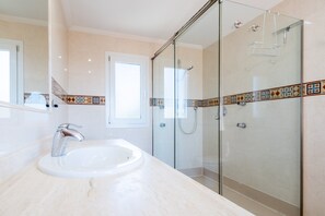 Un baño moderno con cabina de ducha de vidrio, lavamanos con grifo cromado y salpicadero azulejado.