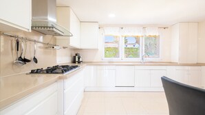 A modern kitchen with white cabinets, a gas stove, and a window with curtains. - Villa 'Can Martinez' with Private Pool, Wi-Fi and Air Conditioning (Llucmajor)