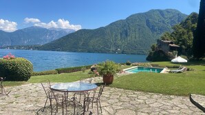 Eine Terrasse am Seeufer mit Tisch und Stühlen, ein Schwimmbecken und ein Berg im Hintergrund.