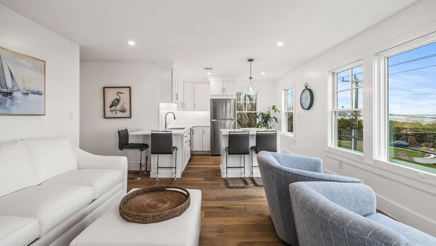 A modern kitchen with white cabinets, stainless steel appliances, and a dining area with two chairs. - Warren House 2BR, Stunning Water Views Downtown (Plymouth)