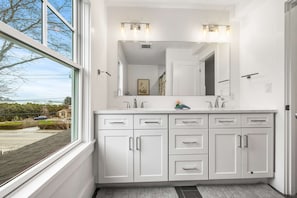A modern bathroom with a large window, a white vanity with multiple drawers, a mirror, and a light fixture above the mirror. - Warren House 2BR, Stunning Water Views Downtown (Plymouth)