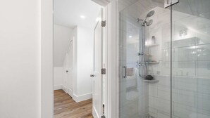 Un baño moderno con cabina de ducha de vidrio, paredes blancas y suelo de madera.